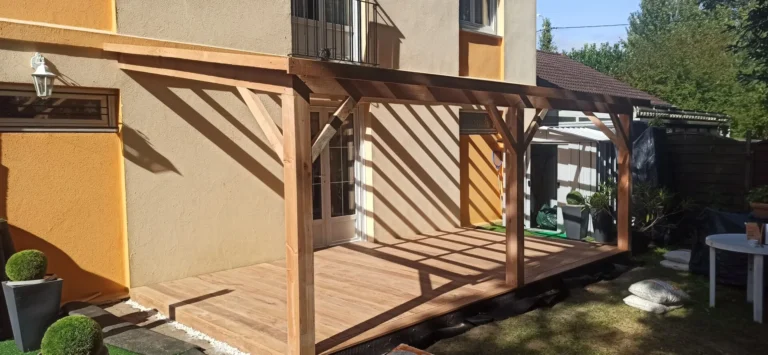 Pergola en bois attachée à une maison, projetant des ombres sur un patio en bois.